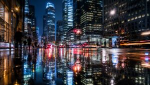 City skyline reflections in wet pavement after rain at night, doubling illuminated buildings and streetlights in symmetrical composition